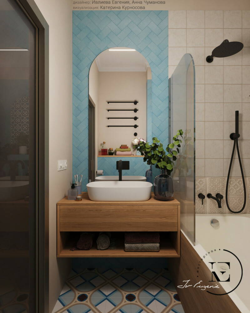 Наличие деревянной тумбы и экрана ванной хорошо передают стилистику  прованса.
Черные элементы смесителей и полотенцасушителя подобраны в тон двери.
Декоративный ряд плитки по периметру ванны очень оживляет.
Полукруглое зеркало поддерживается аркой на противоположной стене.
Изумрудная плитка на стене задает настроение всему помещению.